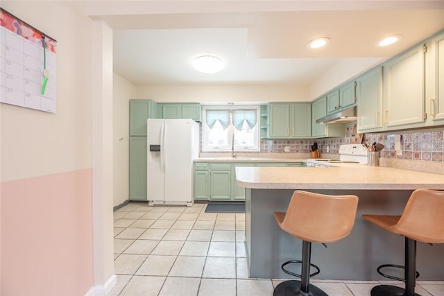 kitchen with white appliances, a kitchen bar, kitchen peninsula, and green cabinets