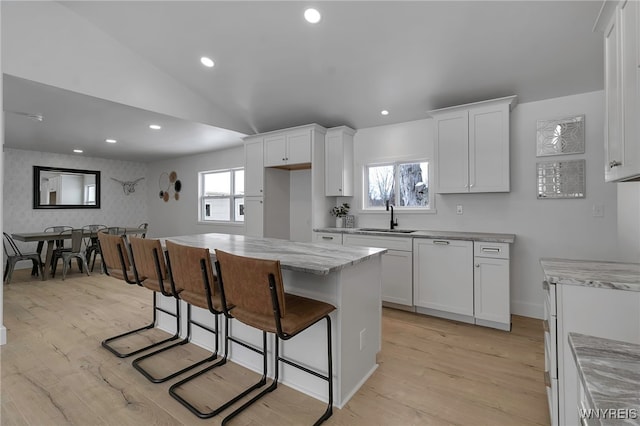 kitchen featuring sink, light stone countertops, a center island, and white cabinets