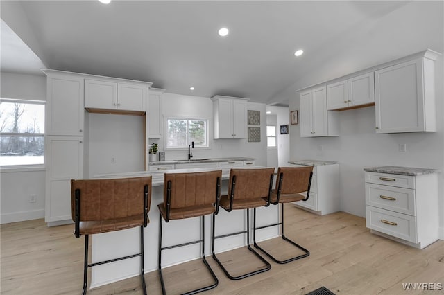 kitchen with white cabinetry, a kitchen island, sink, and light wood-type flooring