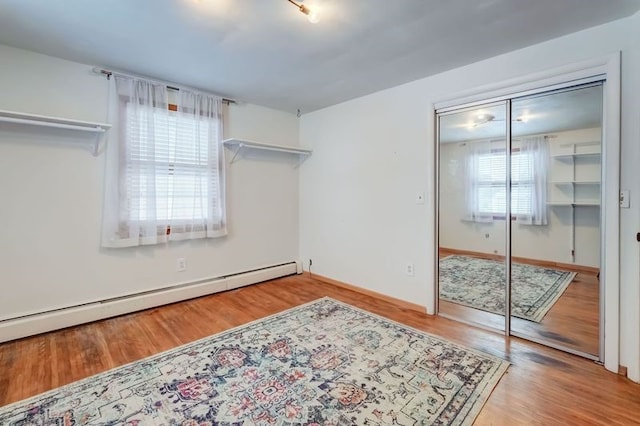 bedroom featuring a closet, a baseboard heating unit, and light hardwood / wood-style flooring