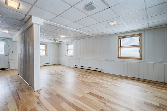 empty room featuring a drop ceiling, light hardwood / wood-style floors, ceiling fan, and baseboard heating