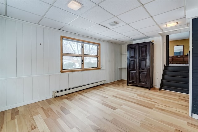 interior space featuring a paneled ceiling, light hardwood / wood-style flooring, and a baseboard heating unit