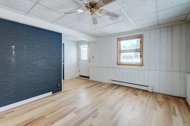 unfurnished room with ceiling fan, light hardwood / wood-style floors, brick wall, and baseboard heating