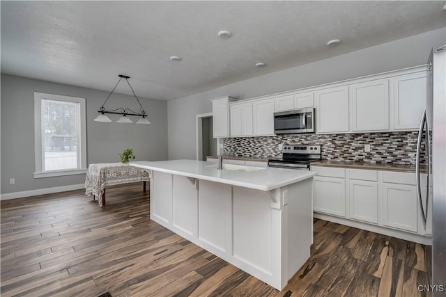 kitchen featuring dark wood-type flooring, white cabinetry, hanging light fixtures, an island with sink, and stainless steel appliances