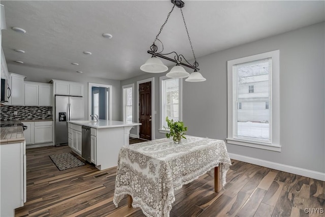 kitchen with pendant lighting, white cabinetry, backsplash, a kitchen island with sink, and stainless steel appliances