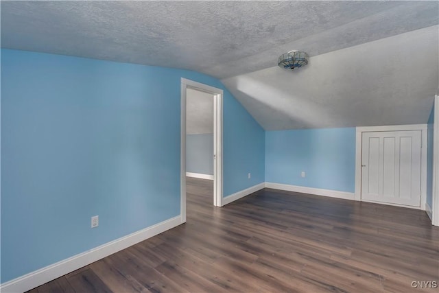 additional living space featuring dark hardwood / wood-style flooring, vaulted ceiling, and a textured ceiling