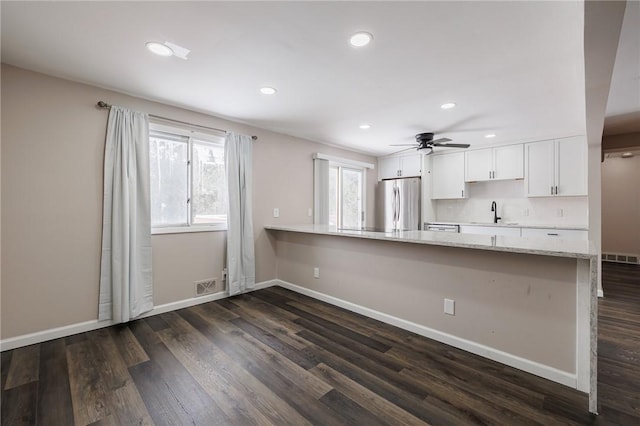 kitchen with white cabinetry, light stone counters, dark hardwood / wood-style flooring, stainless steel fridge, and kitchen peninsula