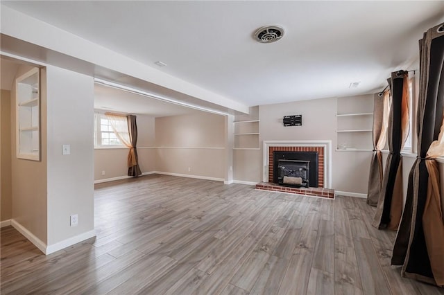 unfurnished living room featuring built in shelves and light wood-type flooring