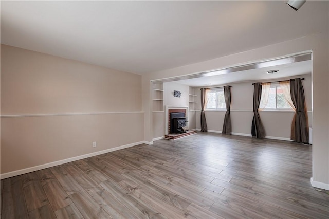 unfurnished living room featuring a brick fireplace, built in features, and light hardwood / wood-style floors