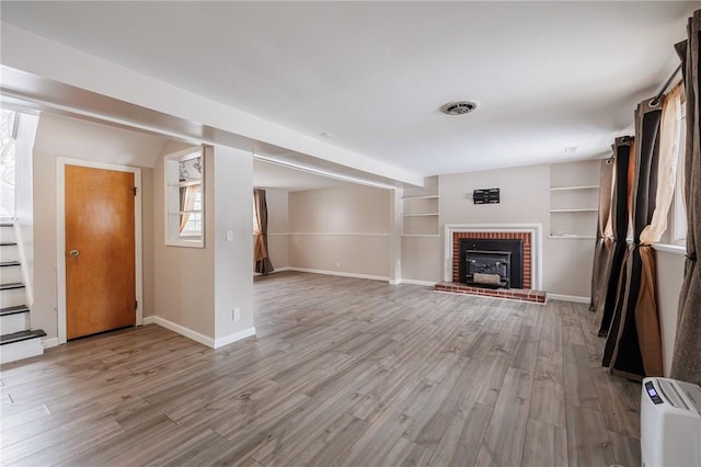 unfurnished living room featuring a brick fireplace, built in shelves, and light hardwood / wood-style flooring