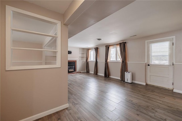 unfurnished living room featuring hardwood / wood-style flooring, a brick fireplace, and built in features