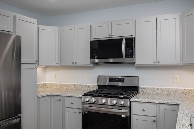 kitchen featuring light stone counters, stainless steel appliances, and gray cabinetry