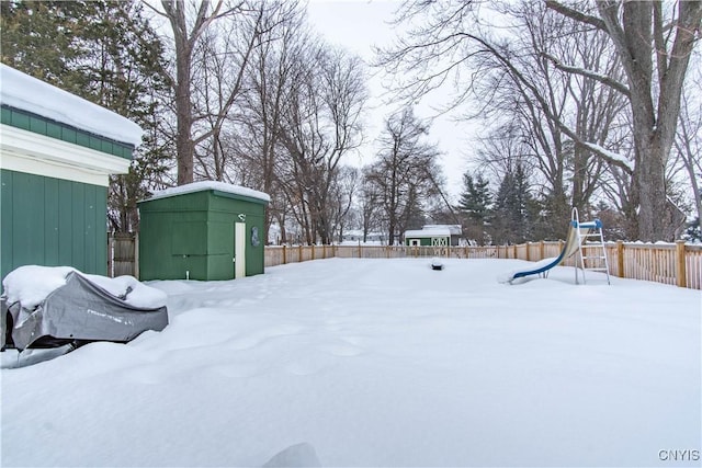 yard layered in snow with a storage shed and a playground