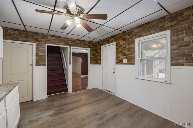 spare room with brick wall, dark hardwood / wood-style floors, a drop ceiling, and ceiling fan