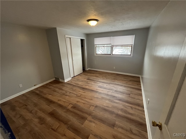 unfurnished bedroom featuring a textured ceiling, dark hardwood / wood-style flooring, and a closet