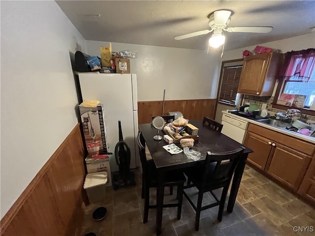 kitchen with dishwasher, sink, ceiling fan, and wood walls