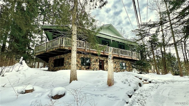 snow covered back of property with a deck, stone siding, and board and batten siding