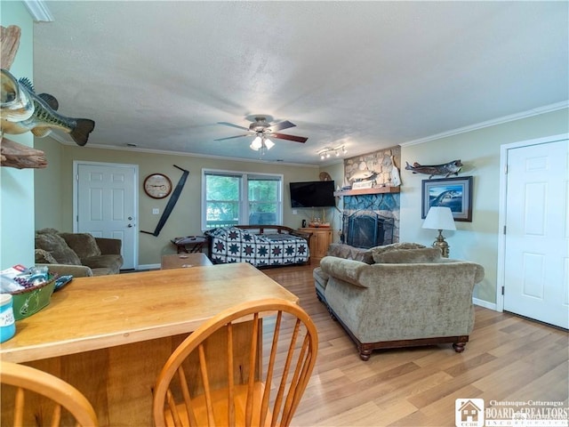 living room with ornamental molding, a stone fireplace, ceiling fan, and light hardwood / wood-style floors