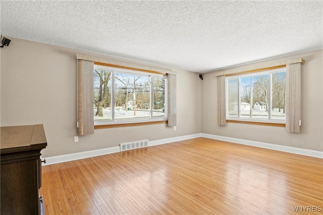 unfurnished room with plenty of natural light, light hardwood / wood-style floors, and a textured ceiling