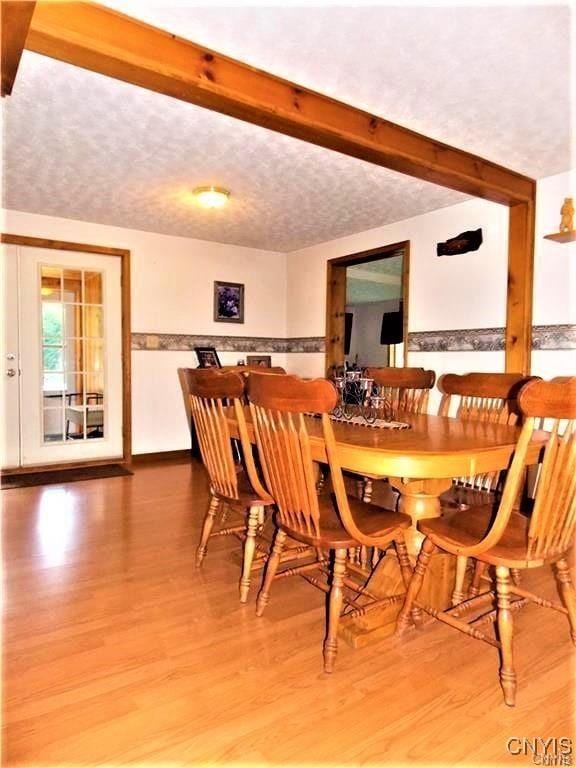 dining space featuring beamed ceiling, wood-type flooring, and a textured ceiling