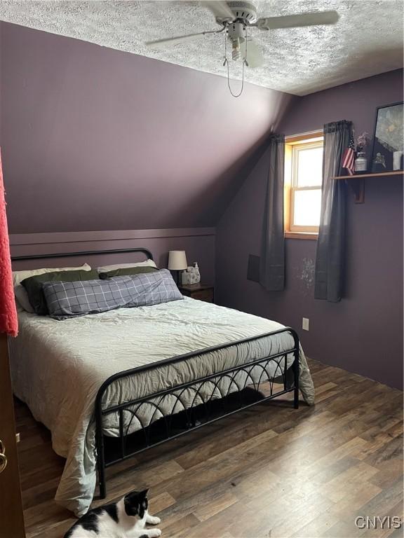 bedroom featuring ceiling fan, lofted ceiling, wood-type flooring, and a textured ceiling