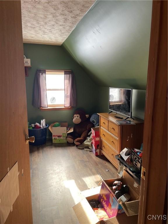 additional living space with hardwood / wood-style flooring, vaulted ceiling, and a textured ceiling