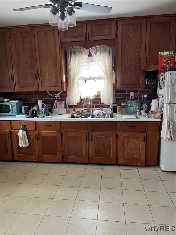 kitchen with sink, light tile patterned floors, ceiling fan, backsplash, and white fridge