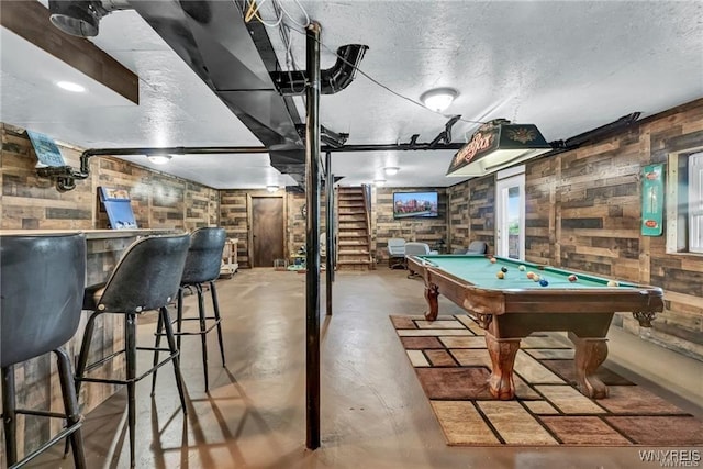 recreation room featuring concrete flooring, a textured ceiling, bar area, pool table, and wood walls