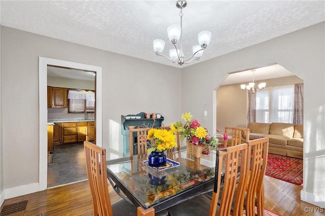 dining area featuring dark wood-type flooring, a chandelier, sink, and a textured ceiling