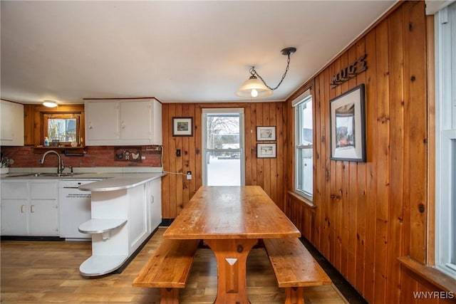 kitchen with pendant lighting, dishwasher, wooden walls, light hardwood / wood-style floors, and white cabinets