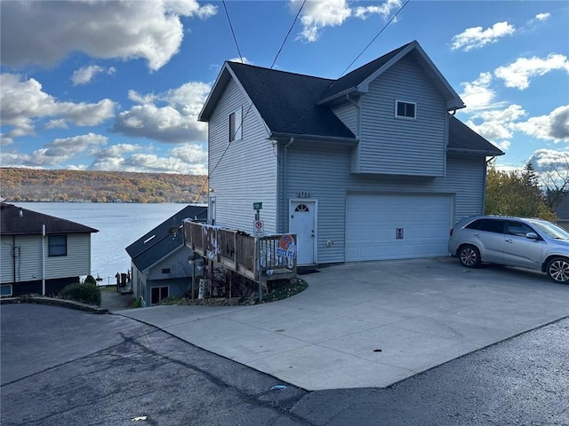 view of property exterior with an attached garage, concrete driveway, a shingled roof, and a water view