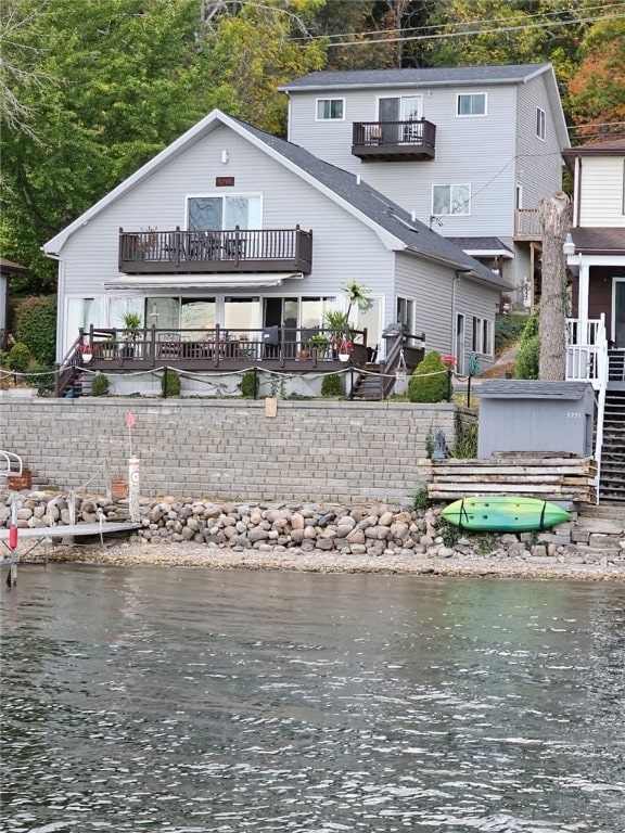 back of house with a balcony, a water view, a hot tub, and stairs