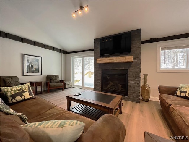 living room with lofted ceiling, a stone fireplace, and light wood-type flooring