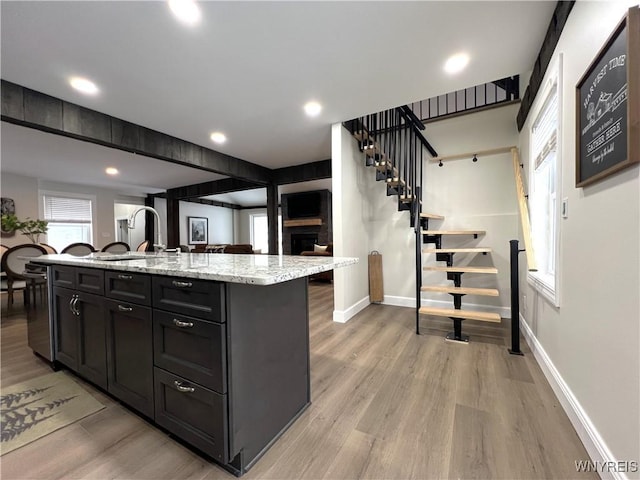 kitchen featuring light stone counters, sink, an island with sink, and light wood-type flooring