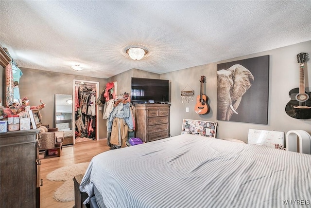 bedroom featuring a walk in closet, light hardwood / wood-style flooring, a closet, and a textured ceiling