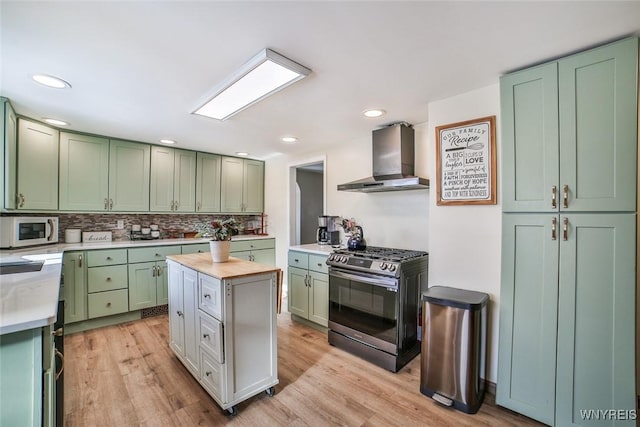 kitchen featuring wall chimney range hood, green cabinets, a center island, and appliances with stainless steel finishes