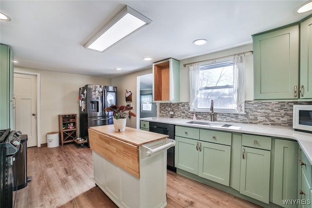 kitchen with sink, stainless steel fridge, range with gas stovetop, green cabinetry, and light wood-type flooring