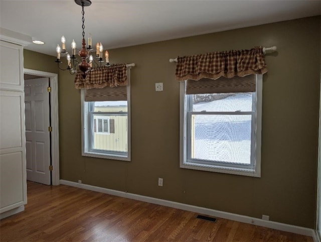 unfurnished dining area featuring an inviting chandelier and hardwood / wood-style floors