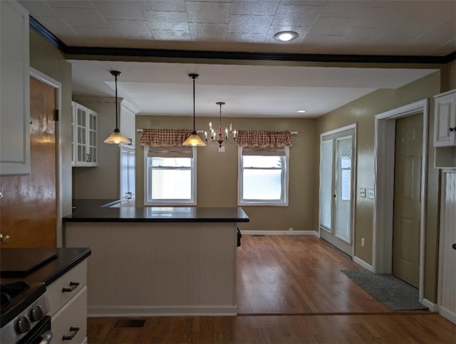 kitchen featuring hardwood / wood-style floors, stainless steel stove, pendant lighting, white cabinets, and a notable chandelier