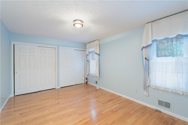 unfurnished bedroom with multiple windows, two closets, and light wood-type flooring