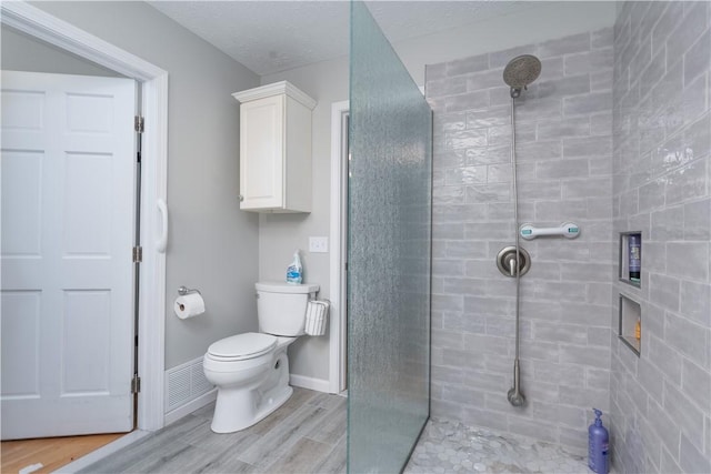 bathroom with hardwood / wood-style floors, a tile shower, a textured ceiling, and toilet