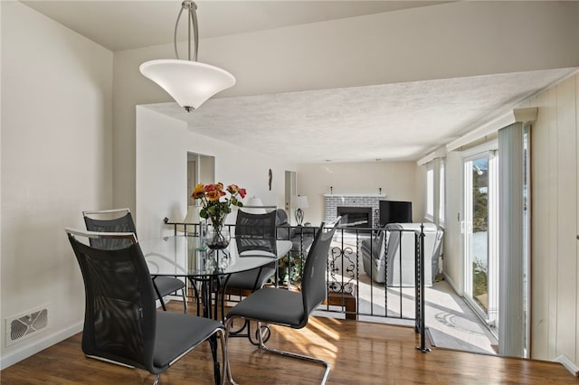 dining space featuring wood-type flooring, a fireplace, and a textured ceiling