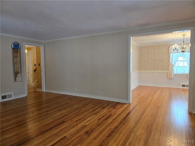 spare room with hardwood / wood-style flooring, ornamental molding, and an inviting chandelier