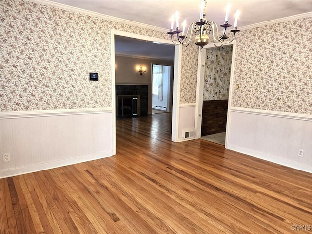 unfurnished dining area featuring crown molding, wood-type flooring, a brick fireplace, and a notable chandelier