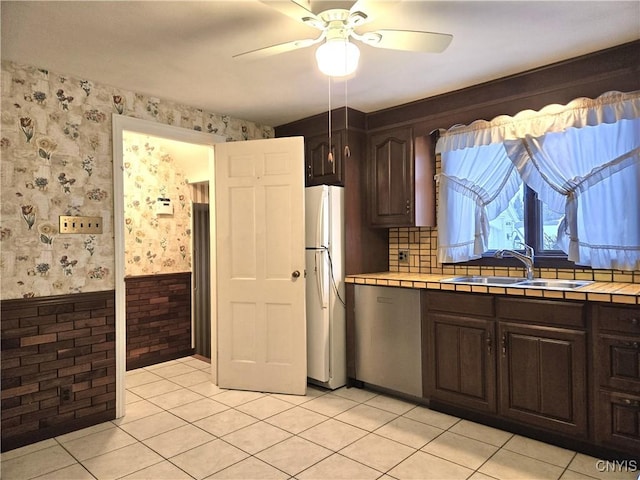 kitchen with sink, dark brown cabinets, tile counters, white fridge, and ceiling fan