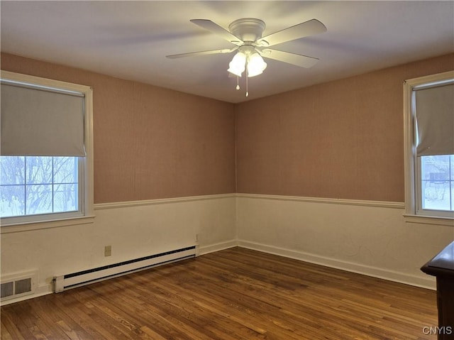 unfurnished room with ceiling fan, a healthy amount of sunlight, dark hardwood / wood-style flooring, and a baseboard heating unit
