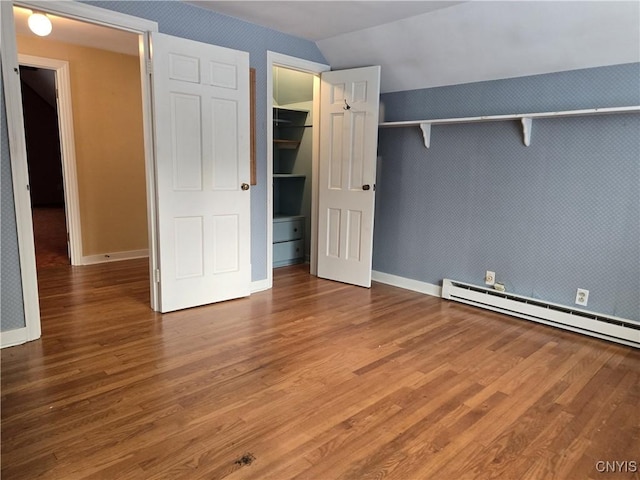 unfurnished bedroom featuring lofted ceiling, a baseboard heating unit, and hardwood / wood-style flooring