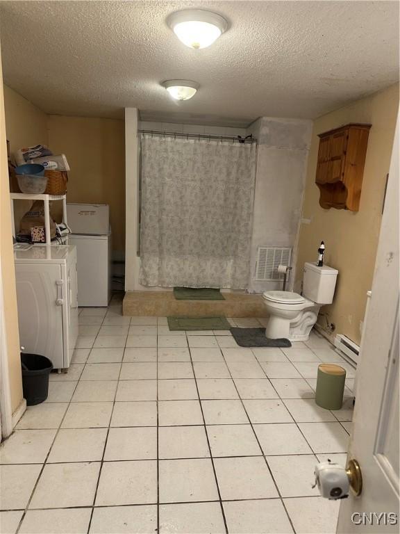 bathroom featuring tile patterned flooring, baseboard heating, toilet, a textured ceiling, and walk in shower