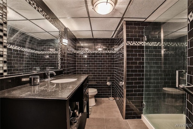 bathroom with tile walls, vanity, a tile shower, tile patterned floors, and toilet