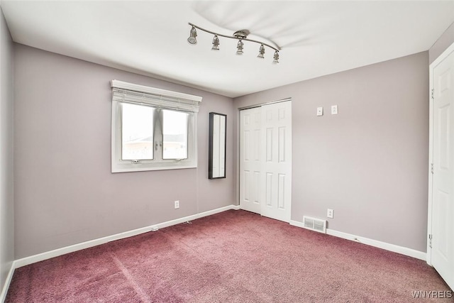 unfurnished bedroom featuring carpet, track lighting, and a closet